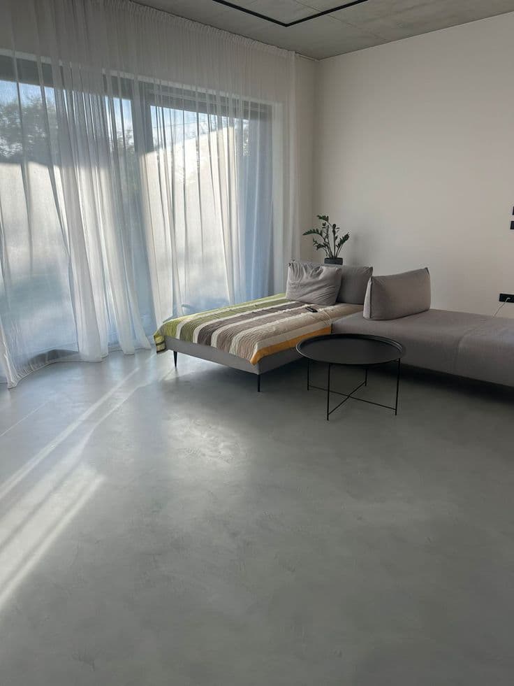 Seamless Microcement Flooring for Living Rooms in Riyadh Light grey matte textured seamless Microcement Flooring installation by Floroz KSA in a modern Riyadh living room with large windows and minimalist furniture.