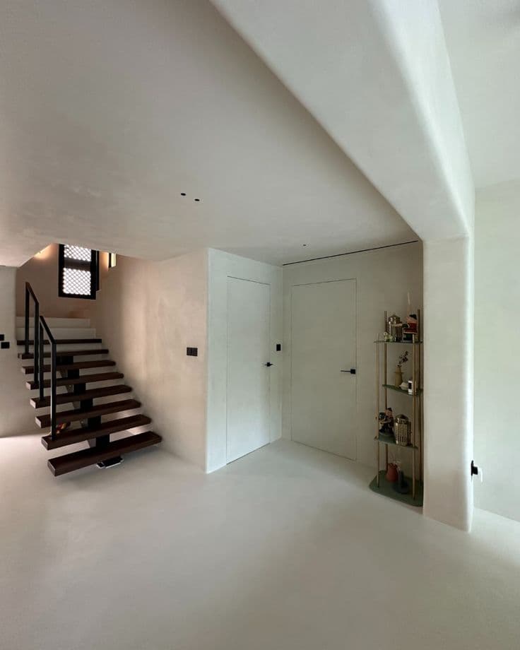 Heavy-Duty Microcement Flooring Villa Entrance in Dammam Seamless off-white matte microcement flooring texture in a modern hallway leading to floating wooden stairs, wear-resistant installation by Floroz KSA.