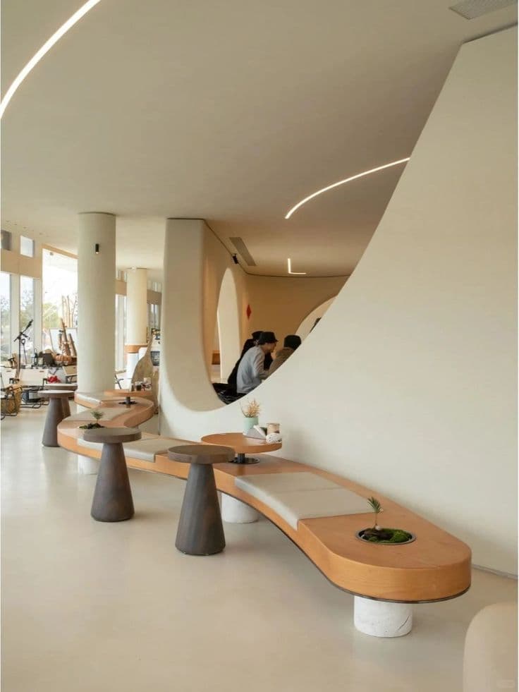 Industrial-Chic Microcement Cafe Flooring in Jeddah Seamless beige matte Microcement Flooring with organic curves in a trendy cafe seating area, featuring curved wooden benches and soft lighting, installation by Floroz KSA.