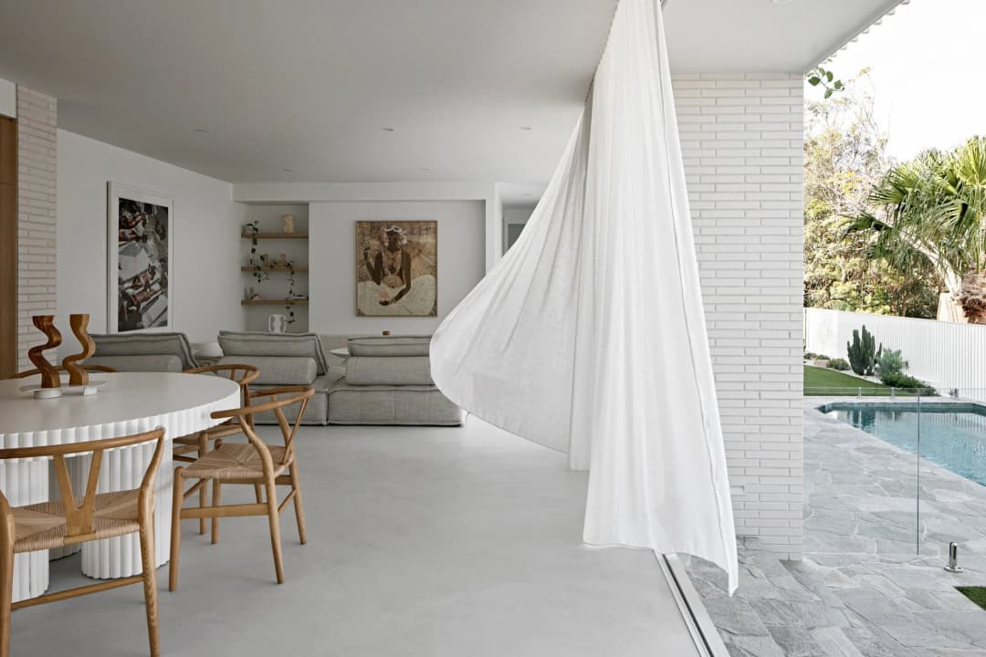 Non-Reflective Matte Flooring for Sunrooms in KSA Bright sunroom dining area featuring non-reflective matte microcement flooring opening directly onto a sunny pool terrace.