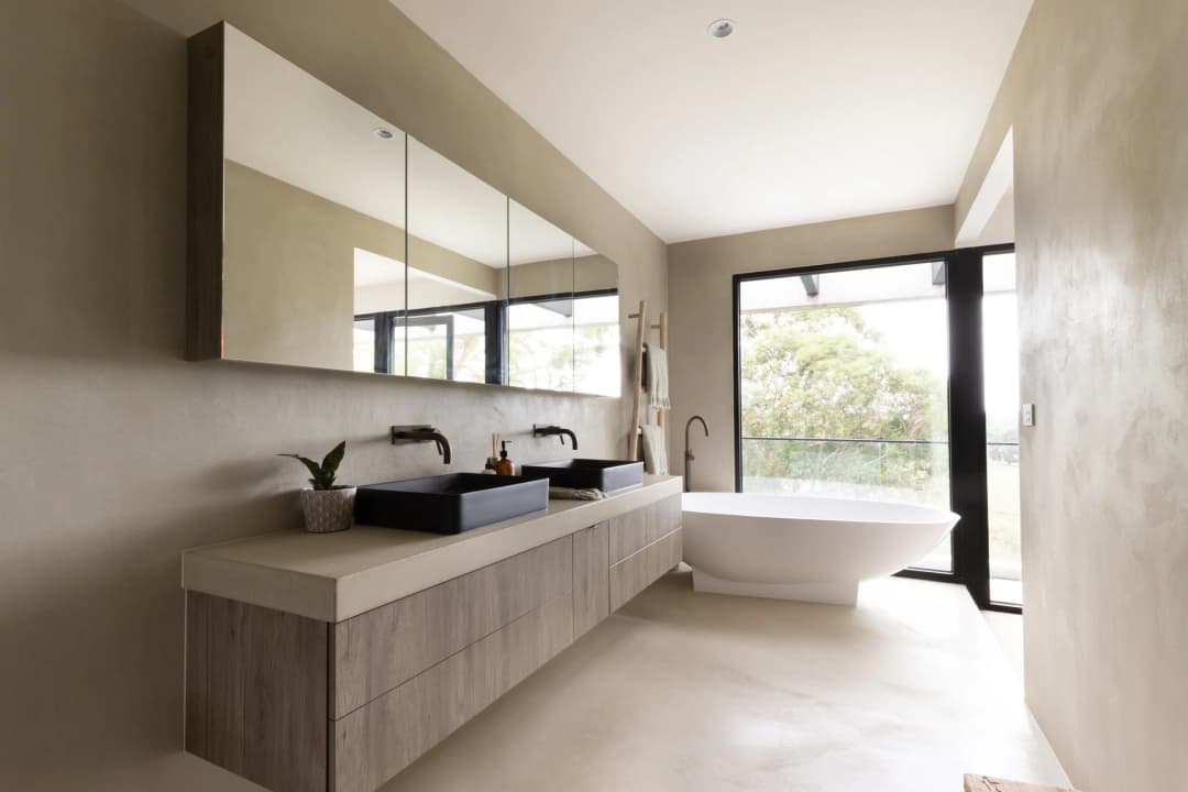Anti-Slip Microcement Flooring for Luxury Bathrooms in Jeddah Luxury bathroom featuring seamless beige microcement applied on both floors and walls, with a freestanding bathtub and black double vanity.
