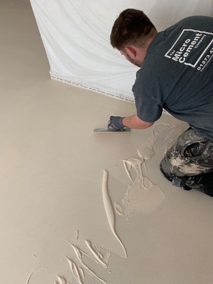 Renovate Without Demolition: Microcement Over Old Tiles in Saudi Homes Professional applicator troweling warm beige microcement over a floor, smoothing the surface to create a seamless finish.